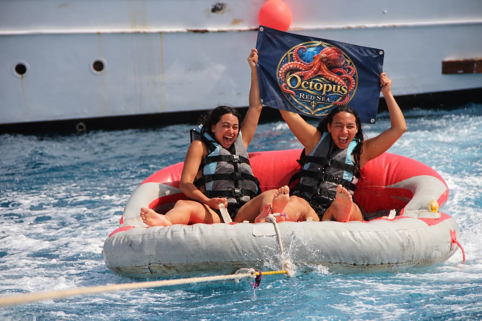 Two friends enjoying a towable water ride and holding an Octopus Red Sea flag