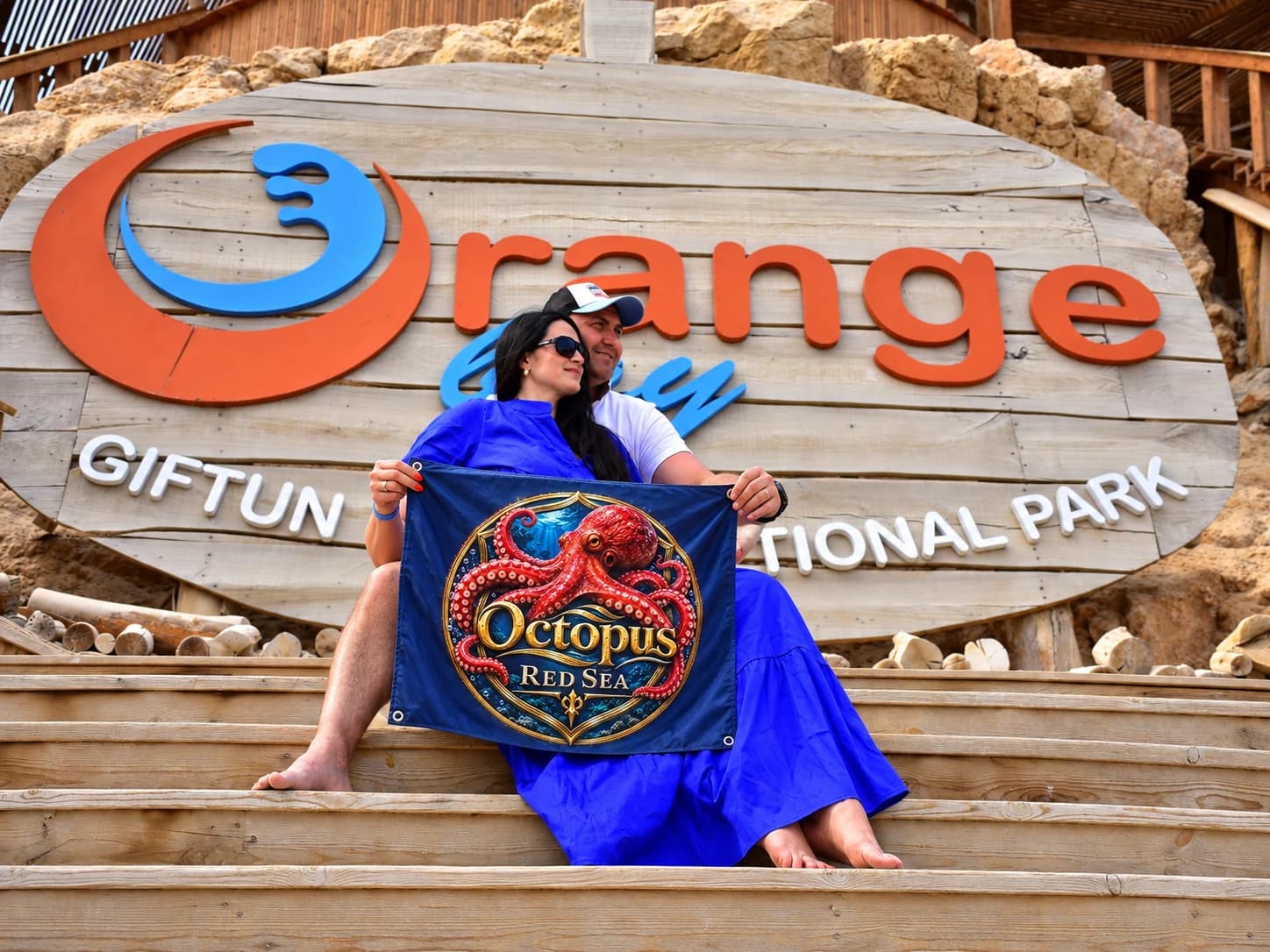 A seated couple with an Octopus Red Sea branded banner at an island beach sign